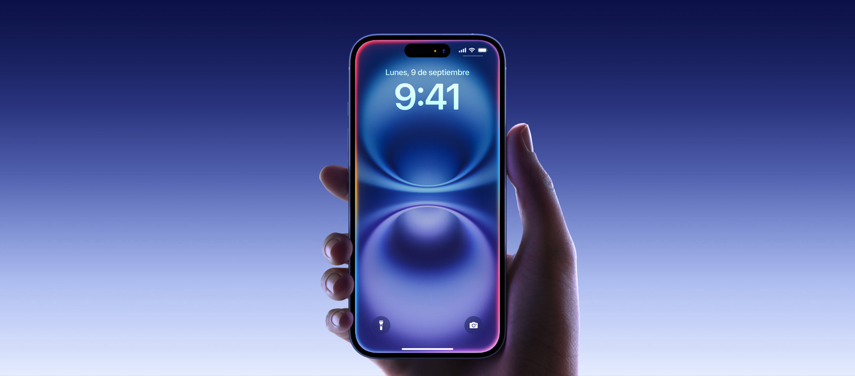 Una mano sujeta un iPhone 16 en azul ultramar que muestra la pantalla de borde a borde, la Dynamic Island centrada en la parte superior y las esquinas redondeadas