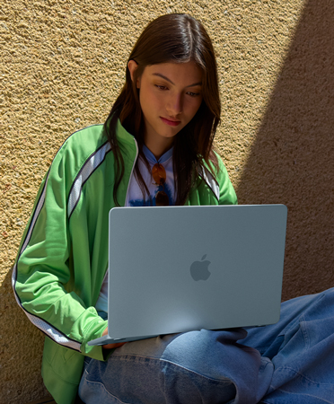 A student sitting outdoors. She has a MacBook on her lap.