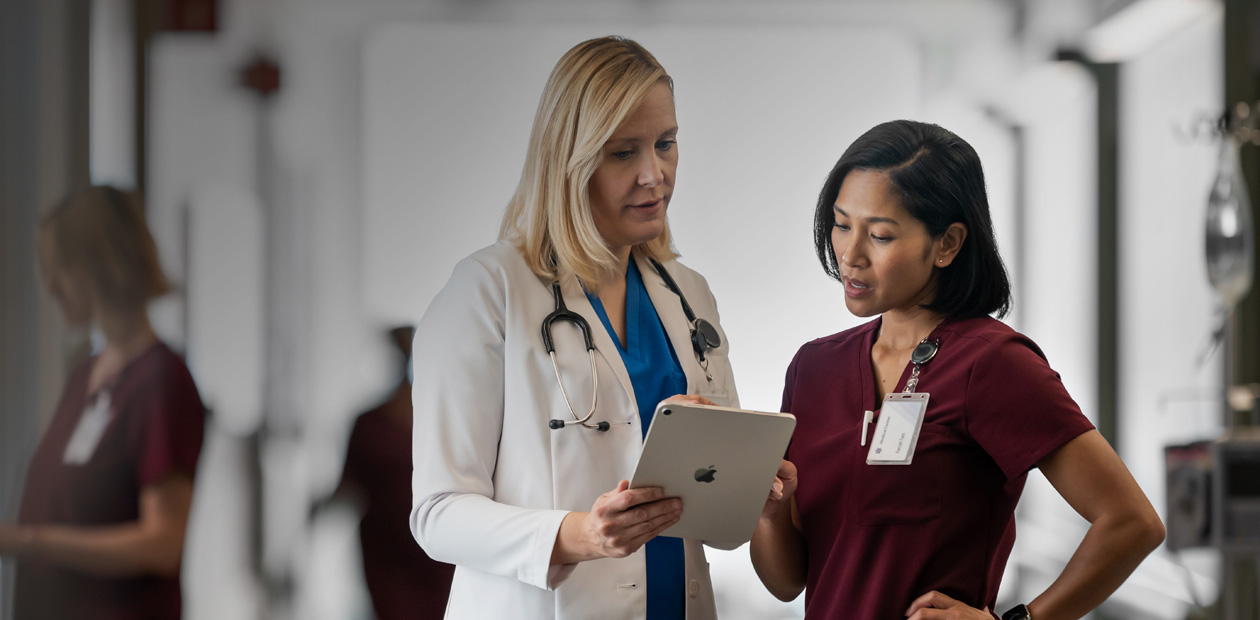 Uma médica e uma enfermeira olhando juntas para um iPad no corredor de um hospital.