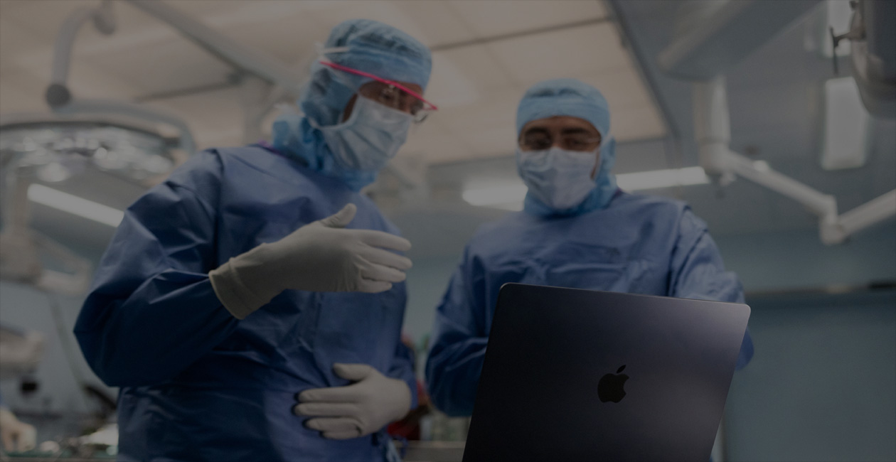 Två kirurger i sjukhuskläder som tittar på en MacBook Pro i en operationssal.
