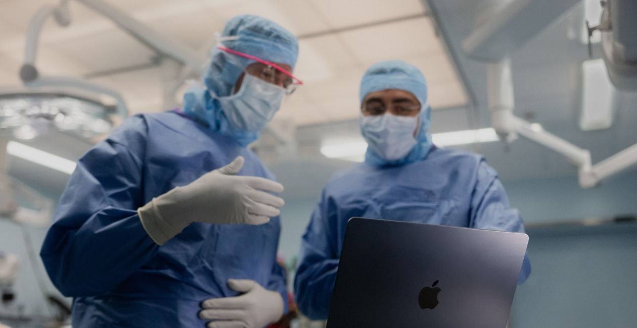 Due chirurghi in sala operatoria parlano di qualcosa rivolti verso lo schermo di un MacBook Pro.