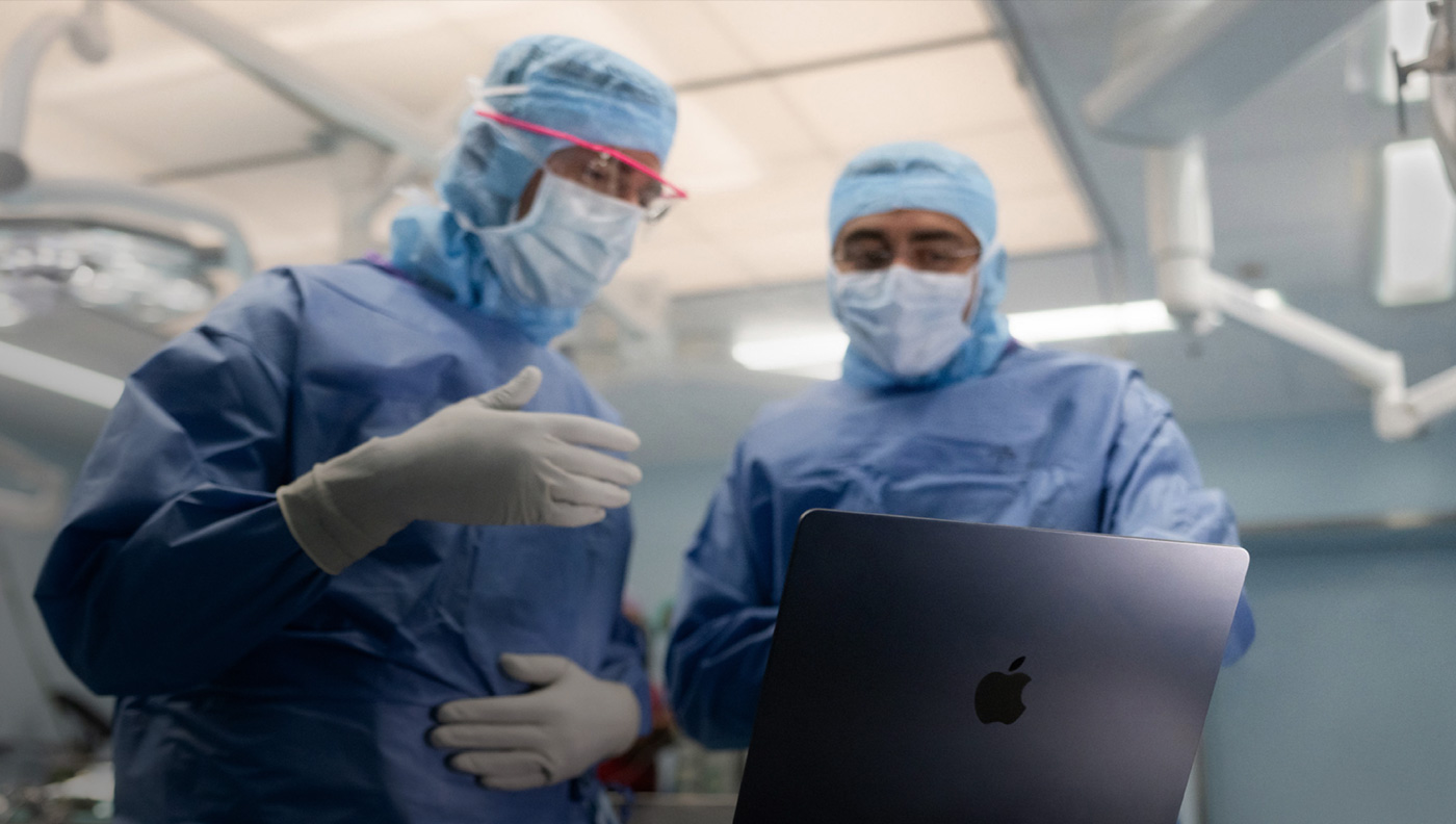 Due chirurghi in sala operatoria parlano di qualcosa rivolti verso lo schermo di un MacBook Pro.