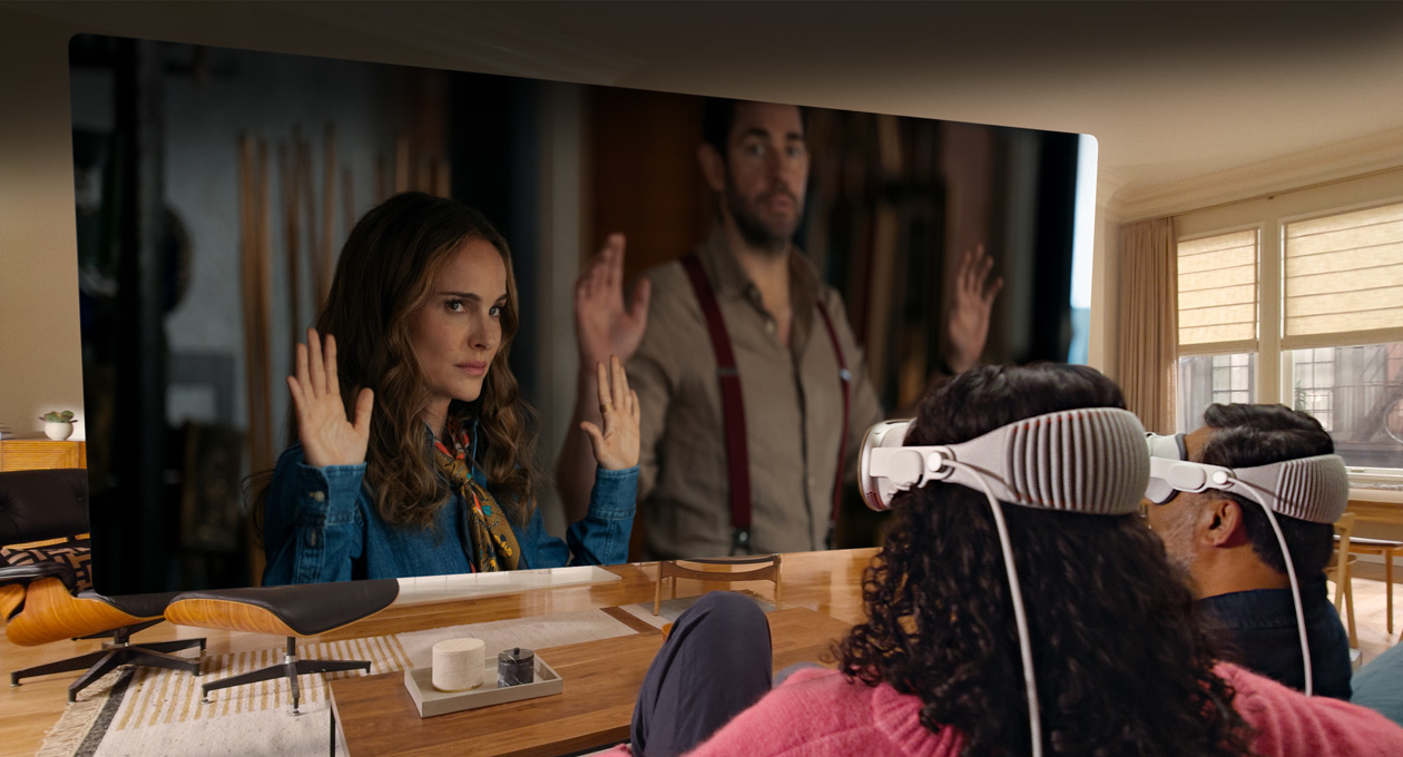 Two people both wearing Apple Vision Pro sit side by side on couch watching: Fountain of Youth movie, displayed on screen stretching across room