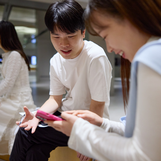 두 사람이 그중 한 명이 들고 조작하고 있는 iPhone을 내려다보며 이야기하는 모습