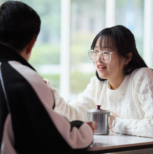 두 사람이 구내식당 테이블에 마주 앉아 이야기를 나누는 모습