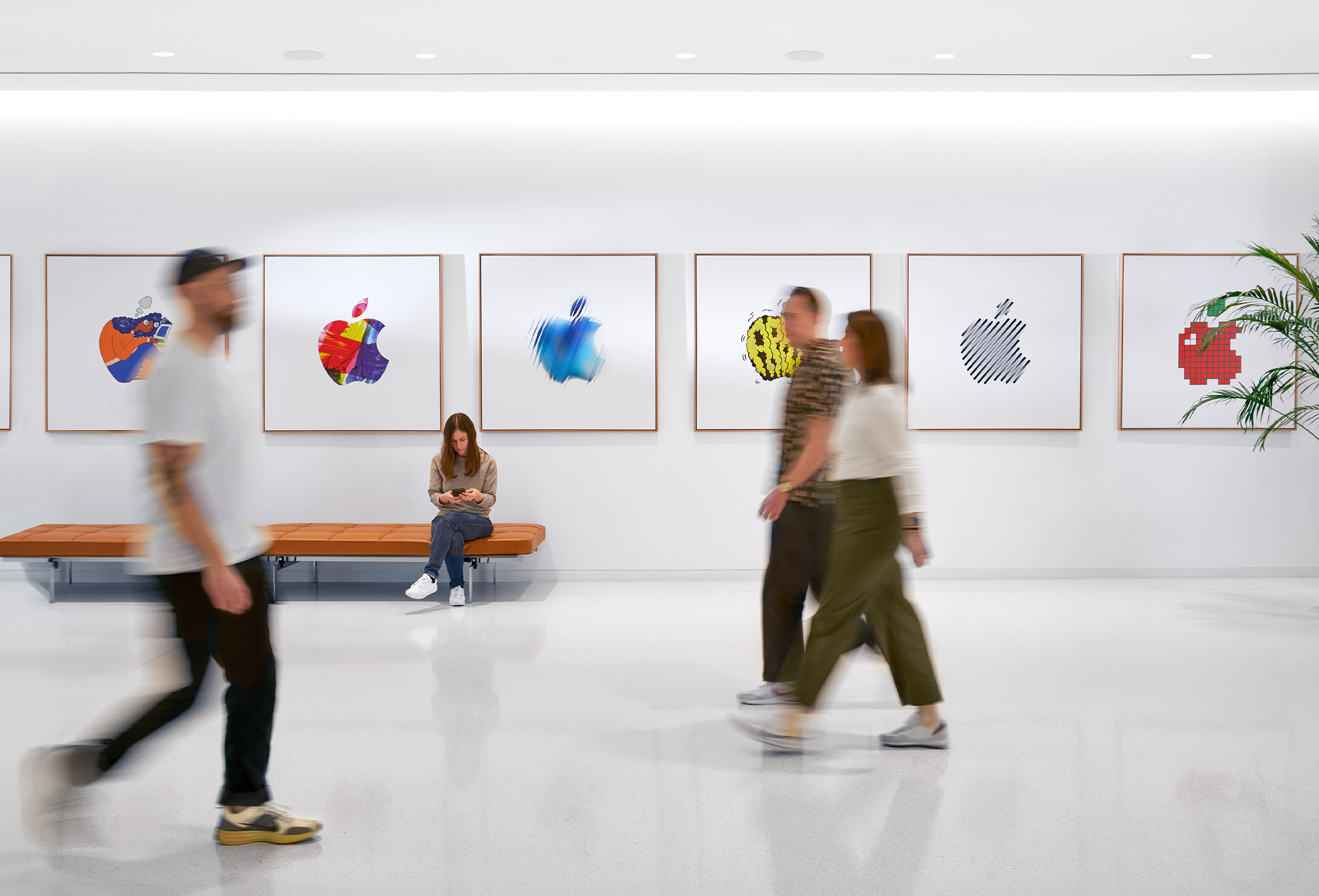 三位 Apple 同事走過佈滿彩色 Apple 標誌的內牆,第四位員工則坐在長椅上。
