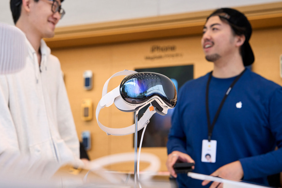 عميل وأحد أعضاء الفريق يتحدثان بالقرب من شاشة Apple Vision Pro في المتجر.