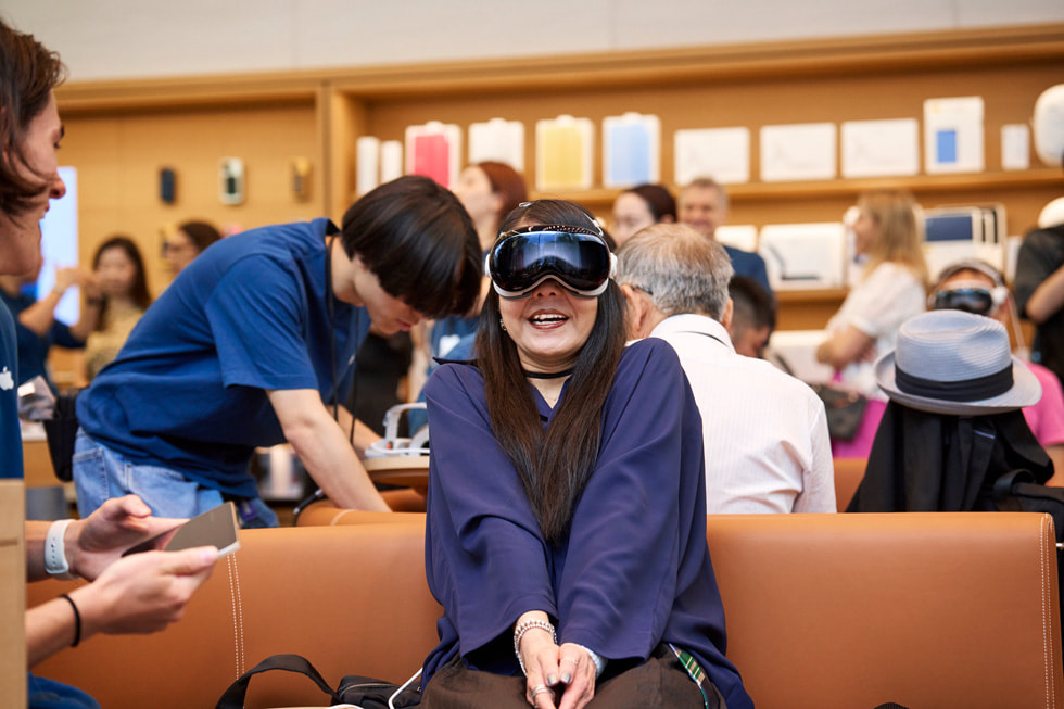 عميلة ترتدي Apple Vision Pro في منطقة العرض التوضيجي في متجر Apple Omotesando وهي تبتسم وتشبك يديها معاً.
