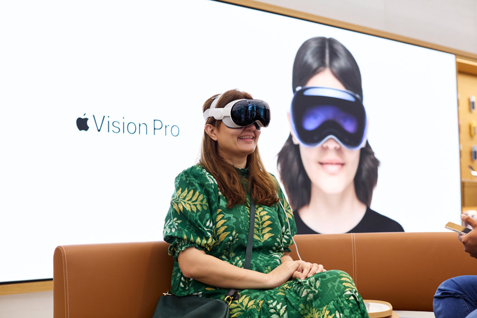 زبونة ترتدي فستاناً أخضر اللون وتجلس وهي ترتدي Apple Vision Pro.