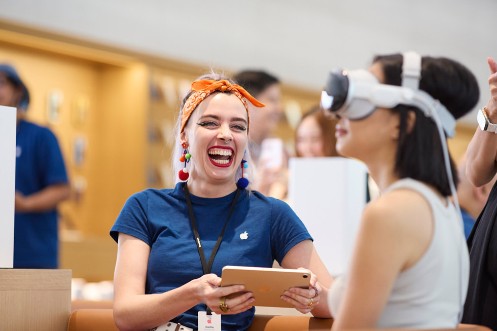إحدى أعضاء الفريق تبتسم ابتسامة عريضة بينما تقوم عميلة بتجربة Apple Vision Pro.