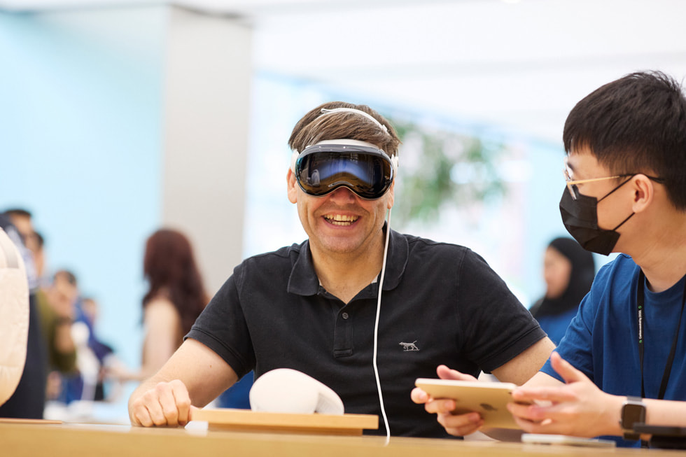 عميل يبتسم أثناء ارتداء Apple Vision Pro بينما ينظر إليه أحد أعضاء الفريق.