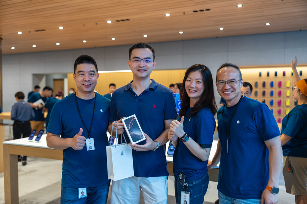 Un client montre son nouvel iPhone 16 tandis que des membres d’équipe de l’Apple Store le félicitent.