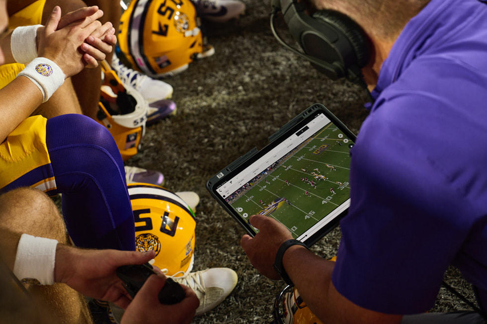Kadra trenerska i zawodnicy drużyny LSU oglądają materiał wideo na iPadzie Pro na linii autowej boiska futbolowego.