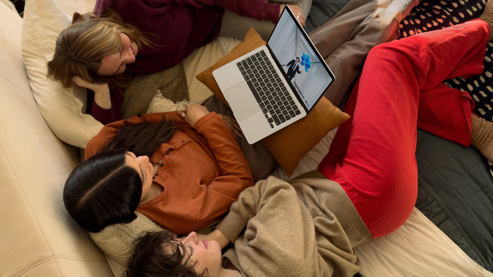 ثلاثة أشخاص يشاهدون مسلسل "Severance" على MacBook Air أثناء جلوسهم على الأريكة.